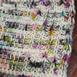Close‑up of a Tunisian crochet swatch in white and multicolored yarn, showing detailed stitch texture along the right edge.