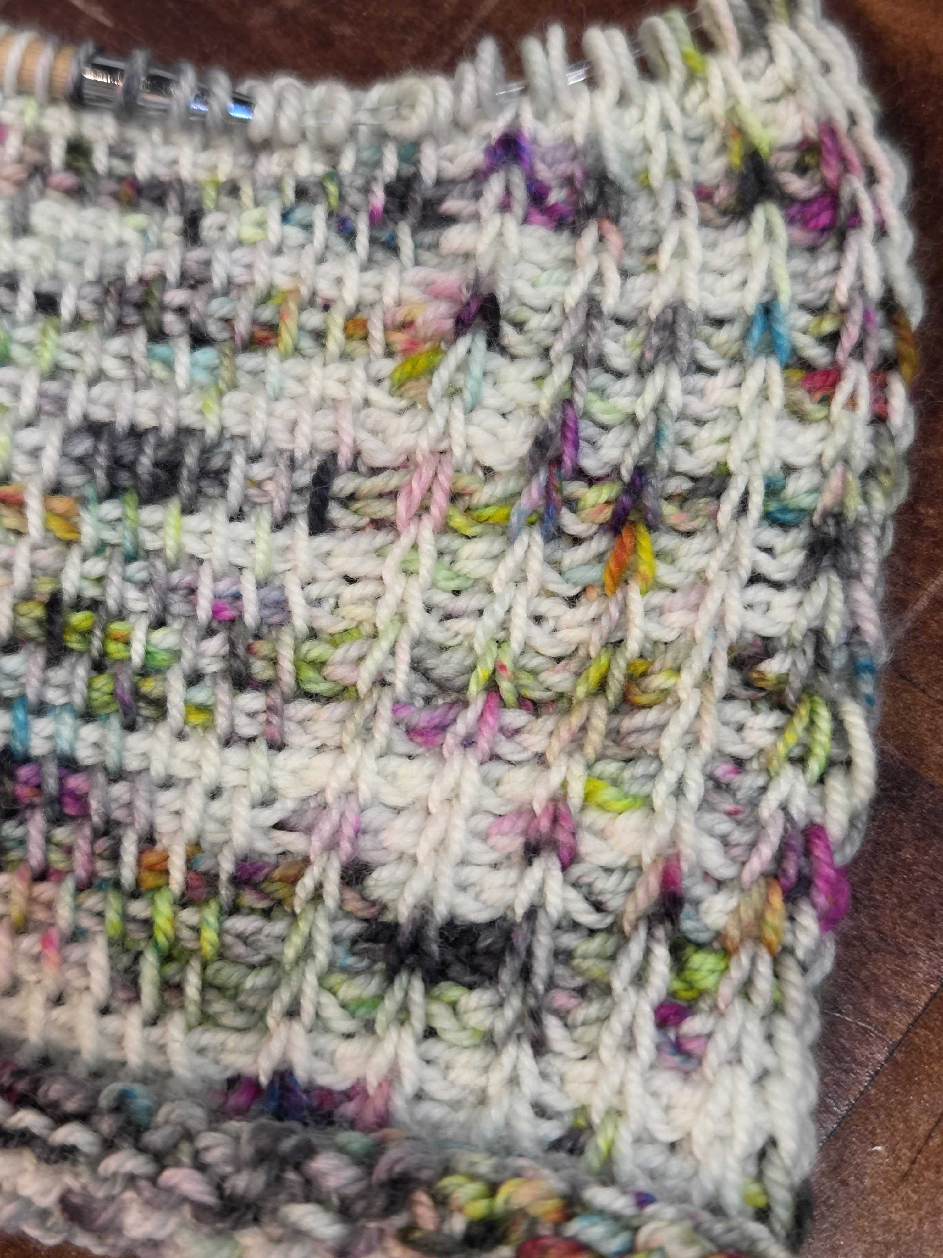Close‑up of a Tunisian crochet swatch in white and multicolored yarn, showing detailed stitch texture along the right edge.