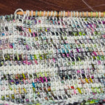 Tunisian crochet swatch in multicolored yarn, shown mid‑row with the hook holding active stitches at the top.
