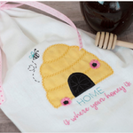 Embroidered bee hive design on a white fabric with honey dipper and jar in the background.
