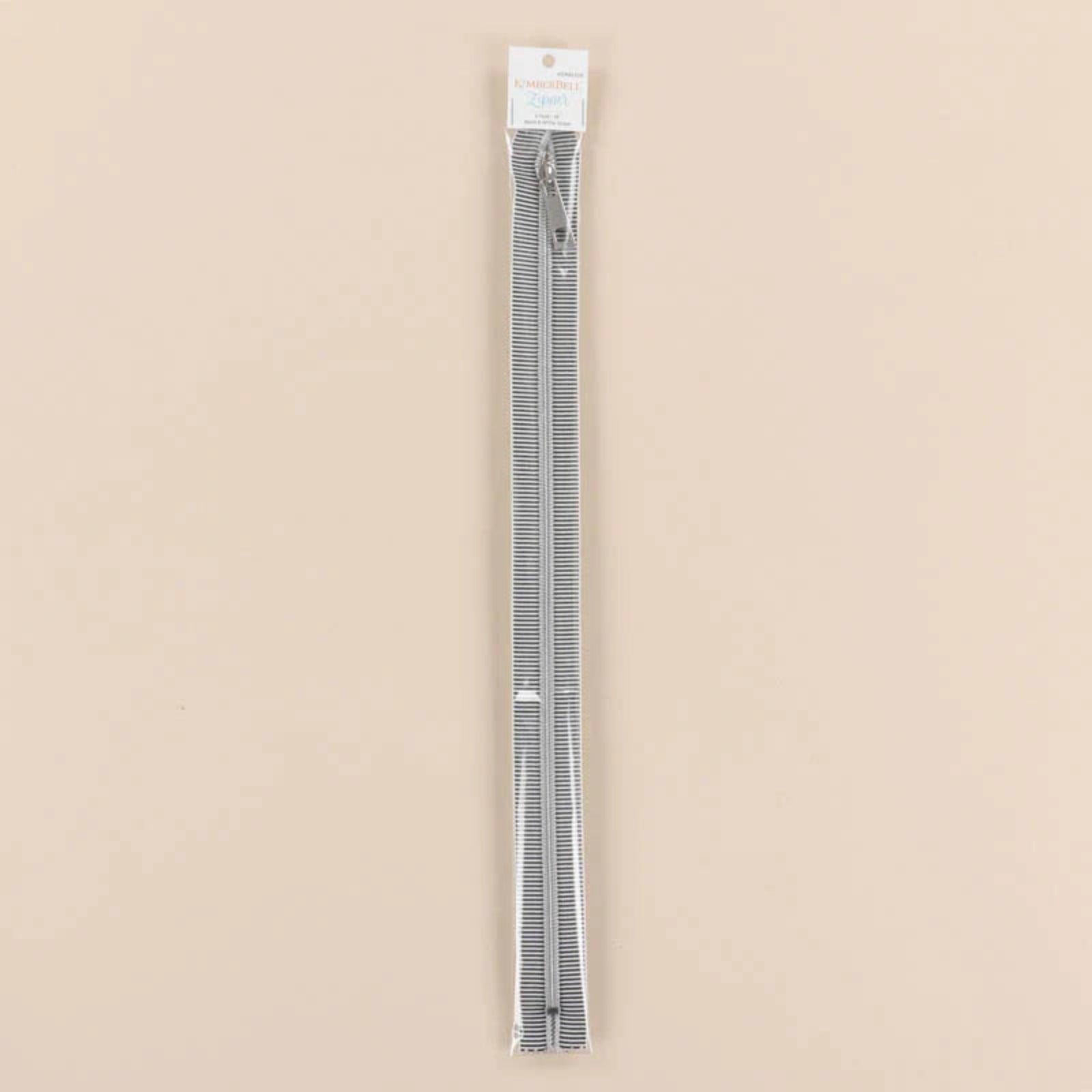 A packaged pair of black and white striped zippers sealed in a clear plastic sleeve with a white header card, set against a solid beige background.