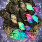 Black hand‑dyed yarn with multicolored neon sections arranged on a dark constellation‑themed background.