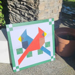 Painted barn quilt featuring two geometric birds in red and blue perched on green squares with a decorative border.