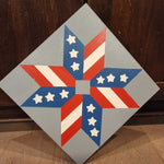 Painted barn quilt featuring a red, white, and blue geometric star design with striped and starred points.