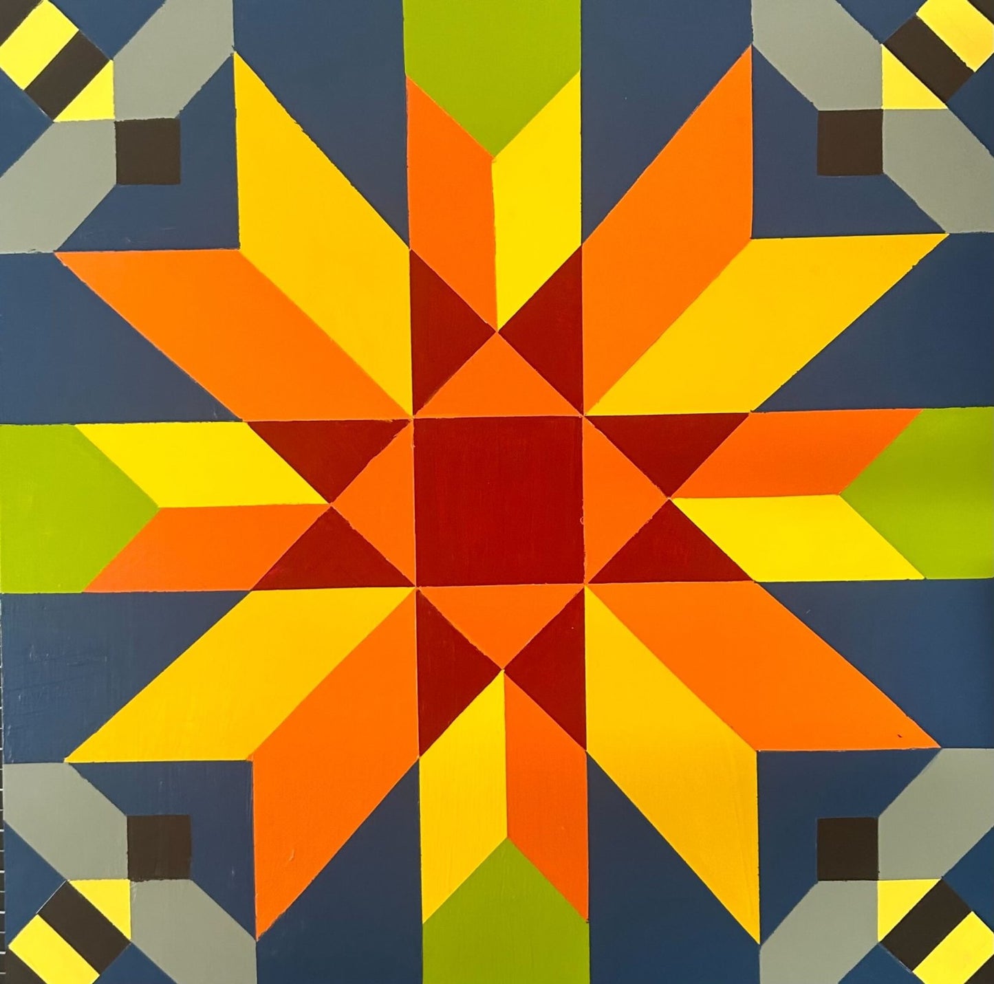 Colorful geometric barn quilt block featuring a red center star with blue, green, yellow, and black accents.