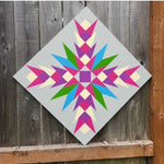 Painted barn quilt featuring a colorful geometric starburst design in pink, purple, green, and blue.