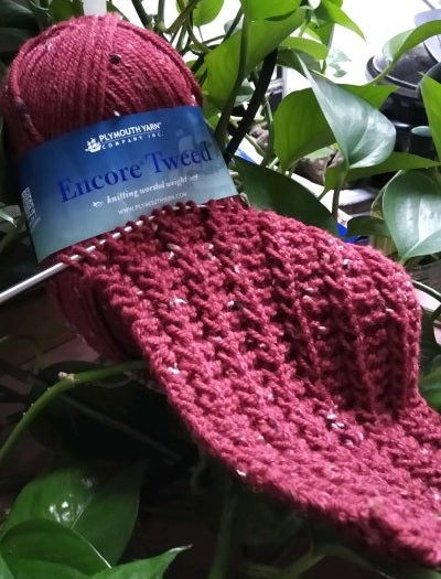 Red tweed yarn and knitting needles working a textured scarf, the project made in Beginning Knitting class.