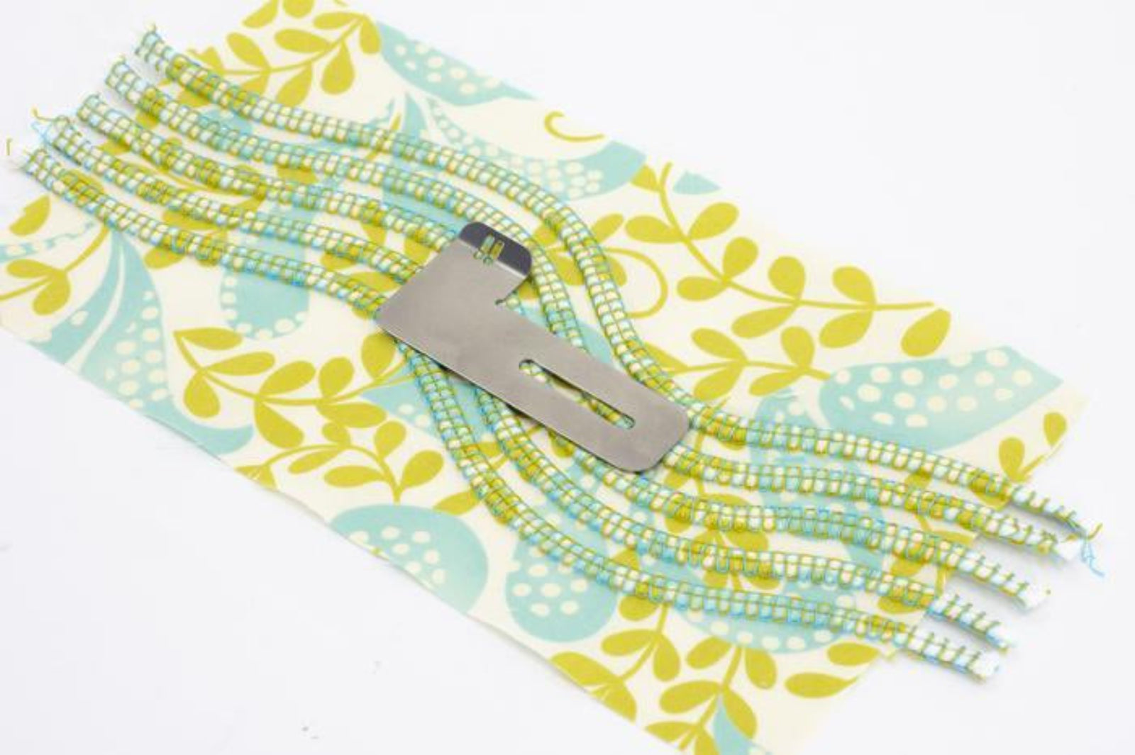 A close-up of a sewing machine presser foot resting on a patterned fabric cover with multiple threads or trim strands extending from it.