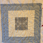 Close-up of a quilt block with blue crosshatch fabric and detailed feather quilting