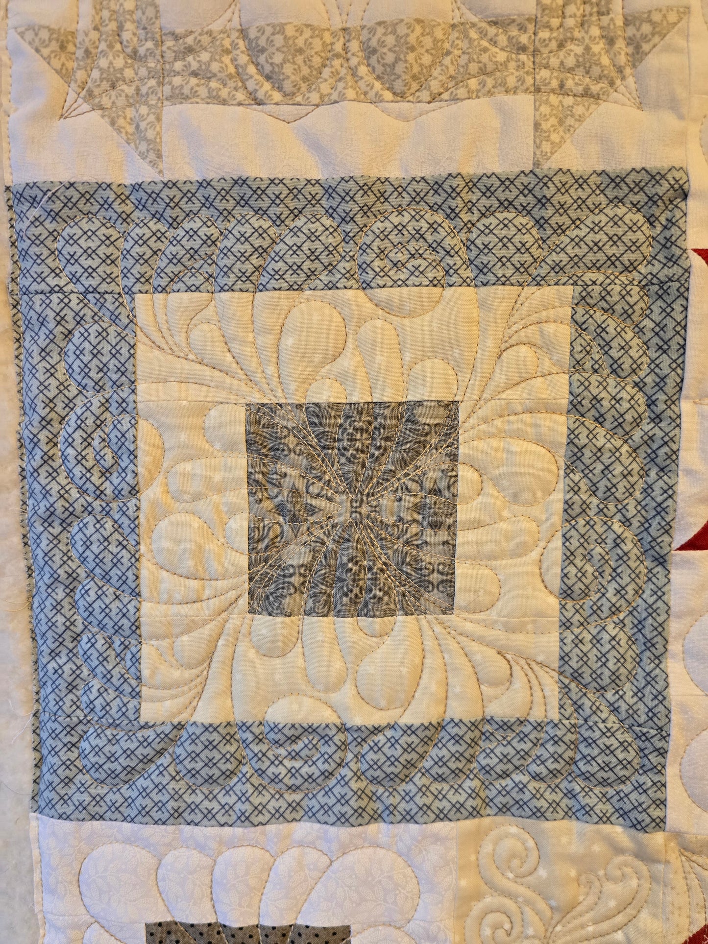 Close-up of a quilt block with blue crosshatch fabric and detailed feather quilting