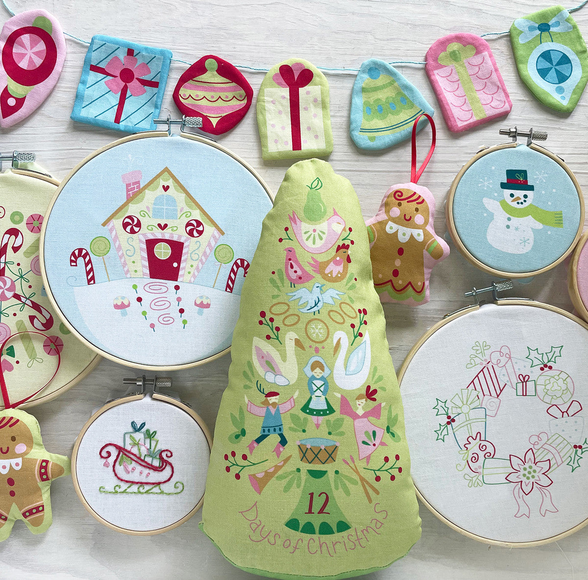 Embroidery hoops with festive designs including gingerbread men, a snowman, and Christmas trees on a white background.