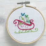 Embroidery hoop with colorful hand embroidered design of a Christmas sleigh on a wooden surface