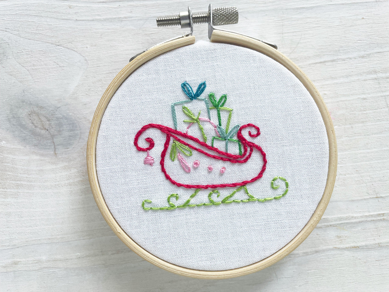 Embroidery hoop with colorful hand embroidered design of a Christmas sleigh on a wooden surface