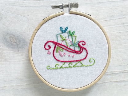 Embroidery hoop with colorful hand embroidered design of a Christmas sleigh on a wooden surface