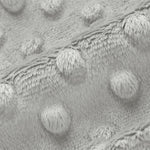Close-up of a light gray textured fabric with raised circular tufted dots and a soft fuzzy border.