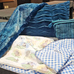Assorted blue Cuddle fabric projects including two blankets, pleated pillow, and zippered pouch laid out on a table.

