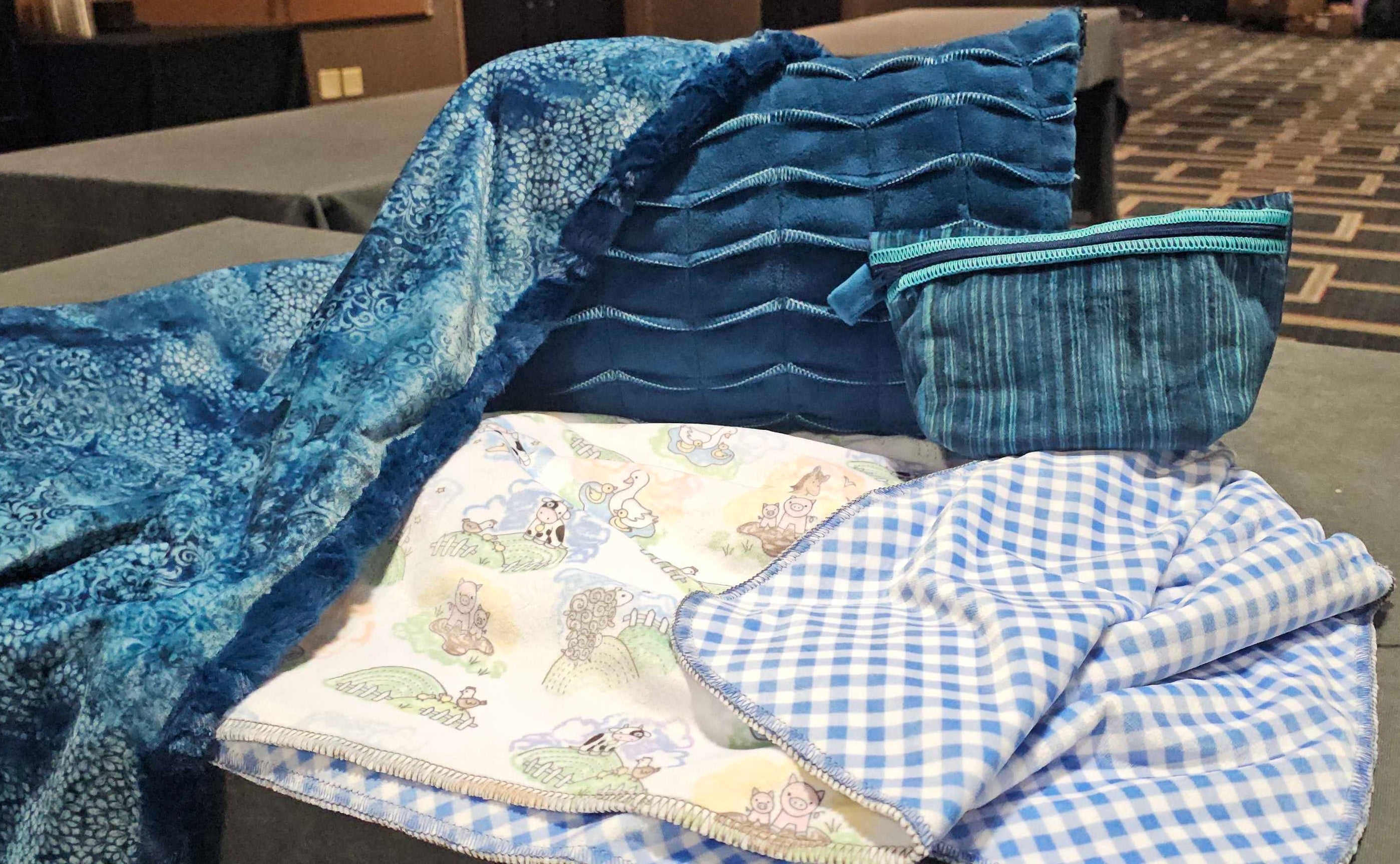 Assorted blue Cuddle fabric projects including two blankets, pleated pillow, and zippered pouch laid out on a table.
