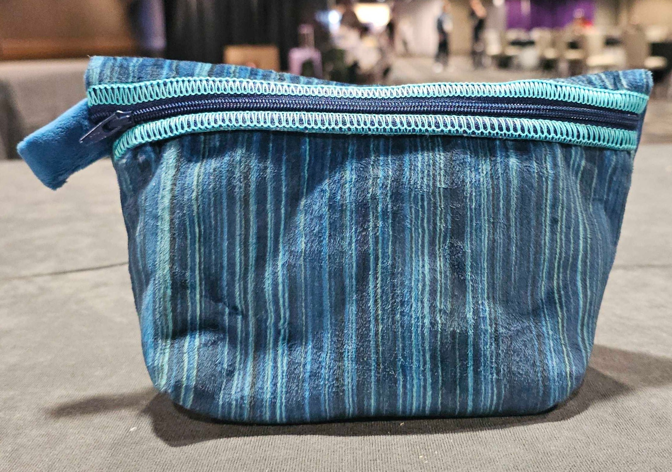 Blue striped Cuddle fabric zippered pouch displayed on a table with the background softly out of focus.