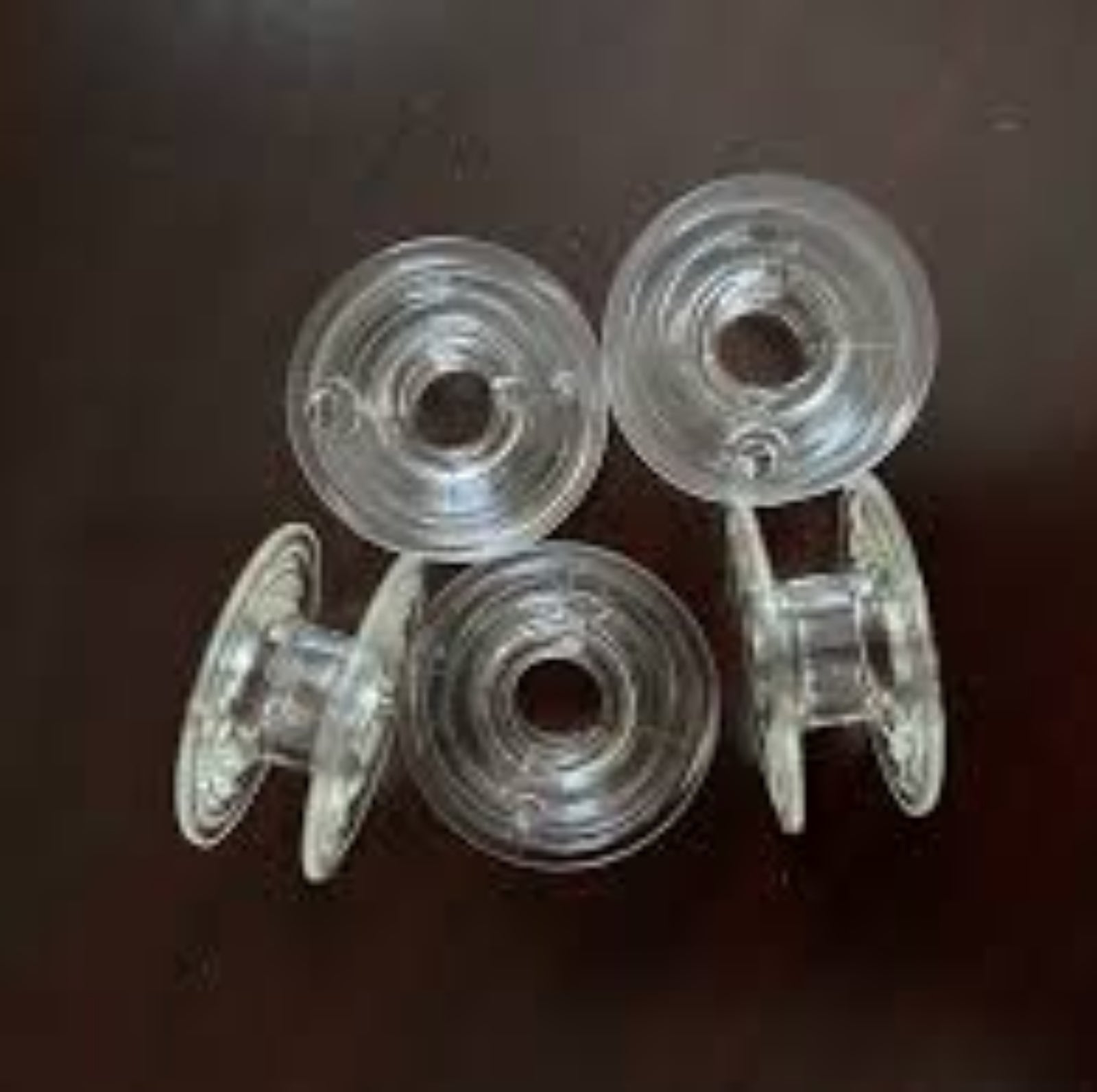 Four clear plastic sewing machine bobbins arranged on a dark brown wooden surface.
