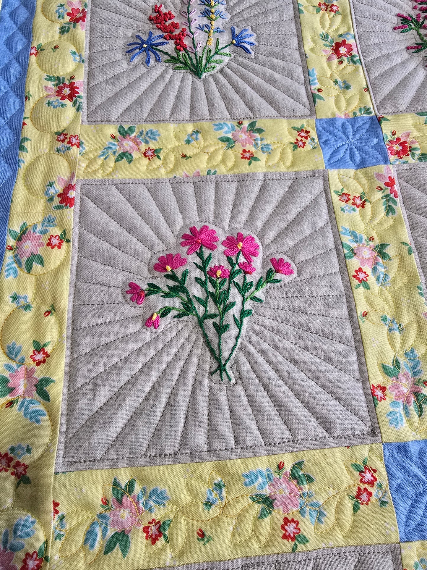 Close-up of embroidered floral quilt blocks with detailed quilting and colorful borders