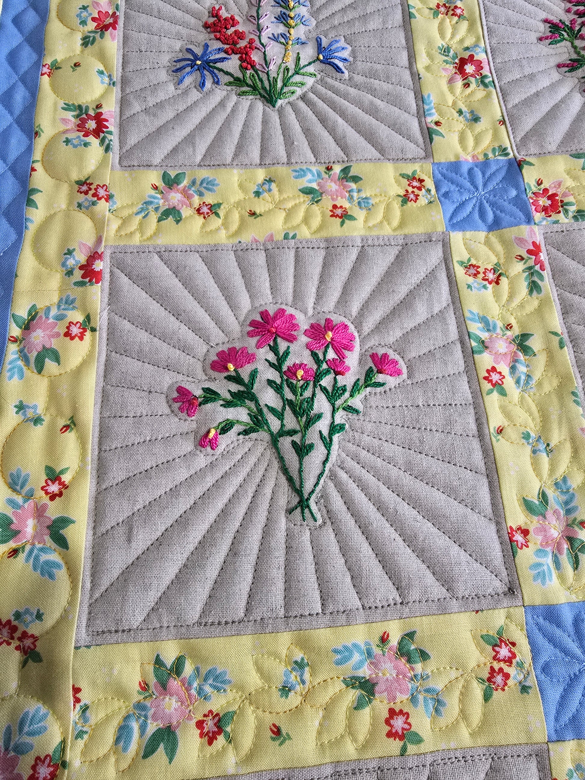 Close-up of embroidered floral quilt blocks with detailed quilting and colorful borders