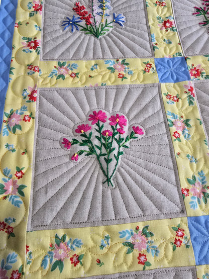 Close-up of embroidered floral quilt blocks with detailed quilting and colorful borders