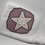 White hand towel with a stitched star design framed by a decorative embroidered border.