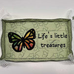 Green fabric tray with lace‑trimmed corners, featuring an embroidered butterfly and the phrase “Life’s little treasures.”