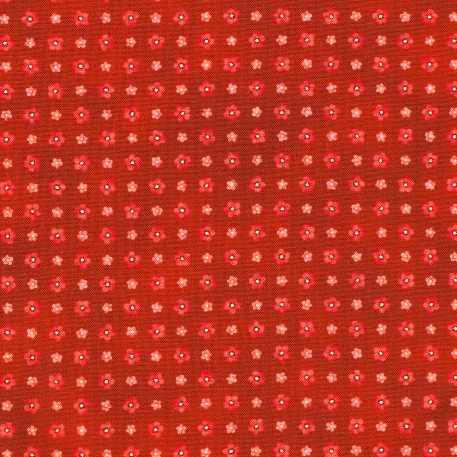 A close-up of a red-orange fabric or material swatch with a repeating small floral pattern in pink, white, and dark red.