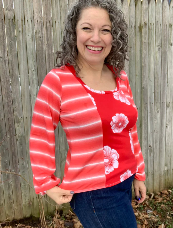 Outdoor view of the long‑sleeve Florence Top featuring a floral front panel with coordinating striped sleeves, shown against a wooden fence backdrop