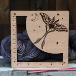 Wooden Luna Moth measuring ruler with engraved celestial details, shown with yarn and knitting needles.