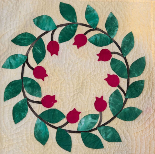 Appliquéd wreath design with green leaves and red motifs on a cream quilted background, used for hand‑quilting practice