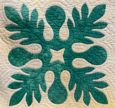 Teal appliqué block with symmetrical leaf shapes on a cream quilted background, used as a hand‑quilting sample.