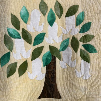 Appliquéd tree with green leaves and white doves on a quilted beige background, used as a hand‑quilting sample.