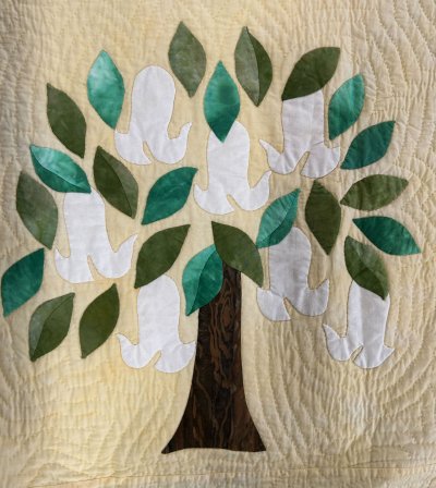 Appliquéd tree with green leaves and white doves on a quilted beige background, used as a hand‑quilting sample.