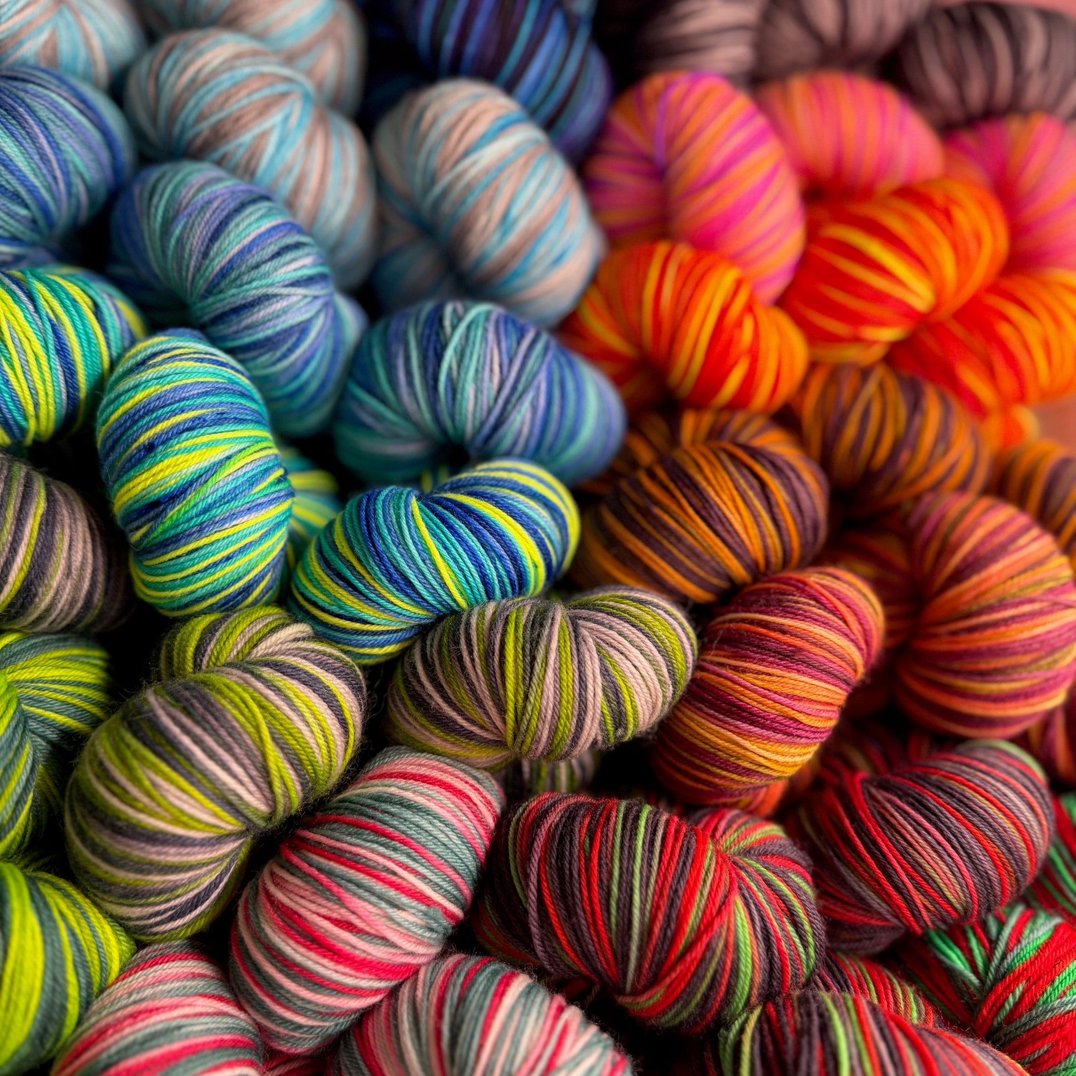 Pile of vibrant multicolored hand‑dyed yarn skeins showing a variety of playful colorways.