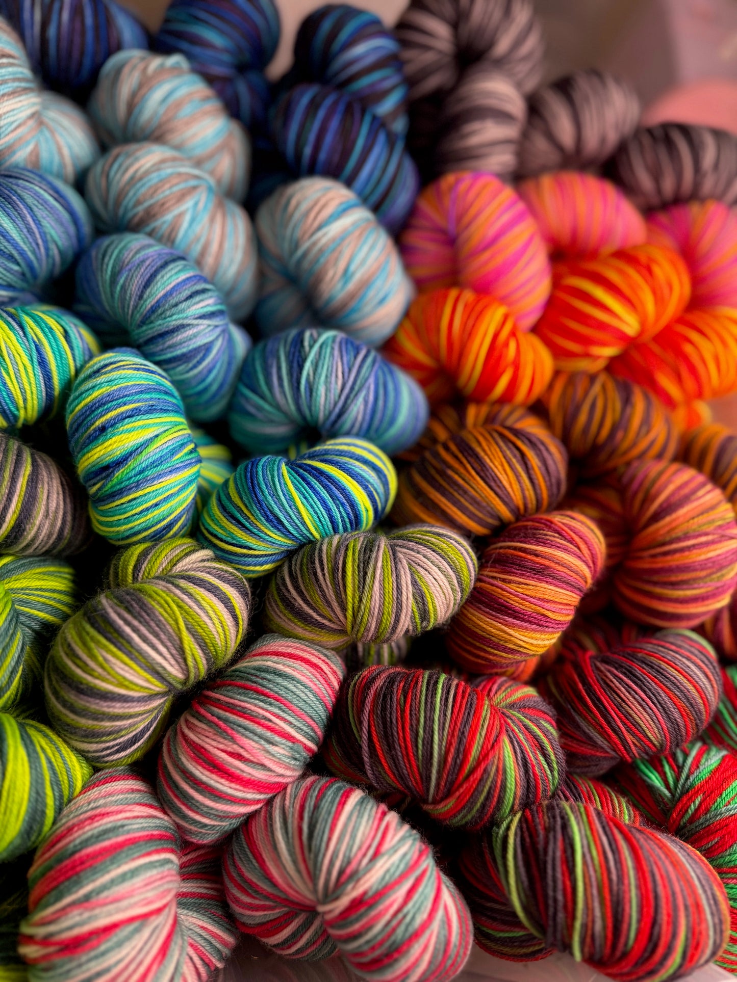 Pile of vibrant multicolored hand‑dyed yarn skeins showing a variety of playful colorways.