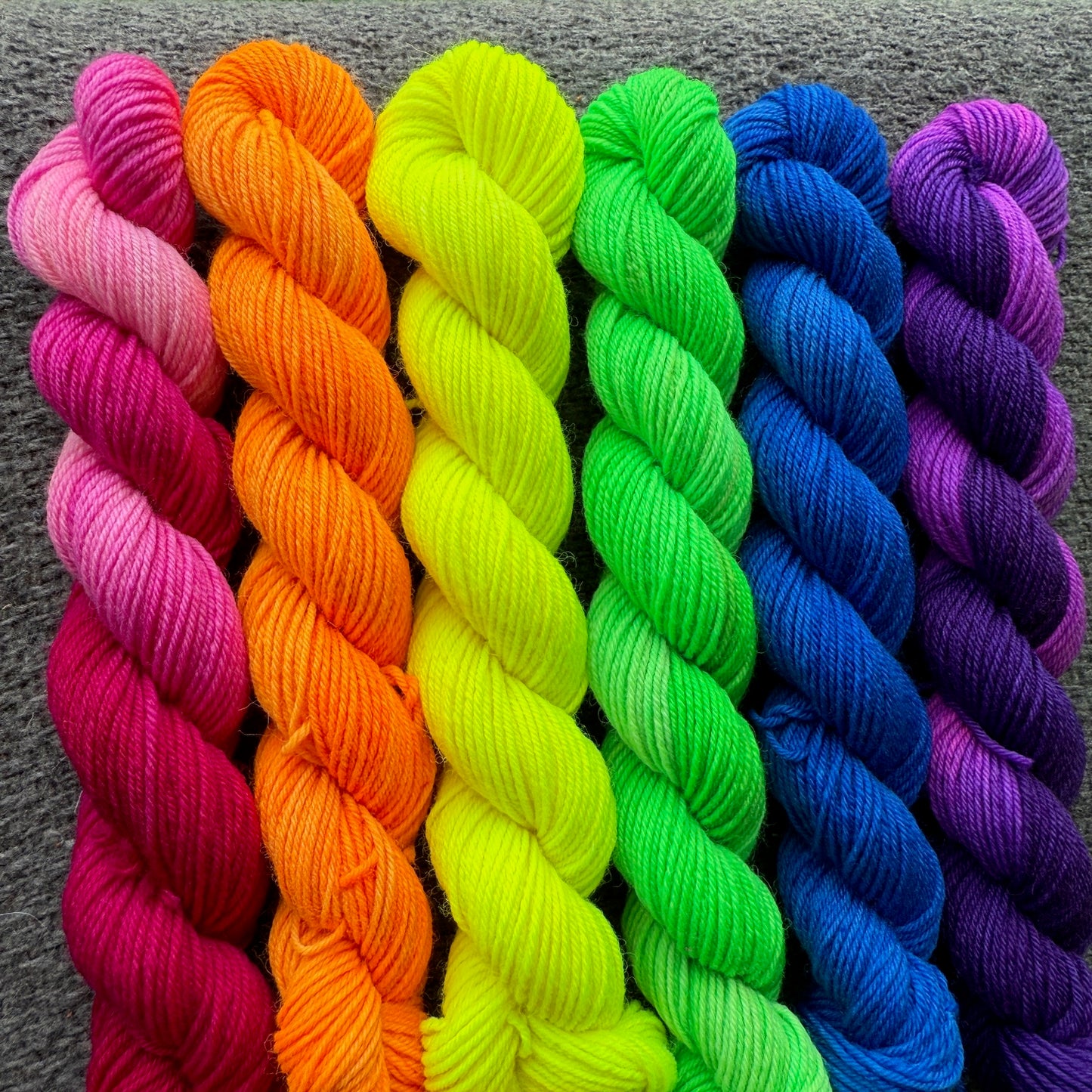 Bright rainbow lineup of six hand‑dyed yarn skeins arranged in a color gradient.