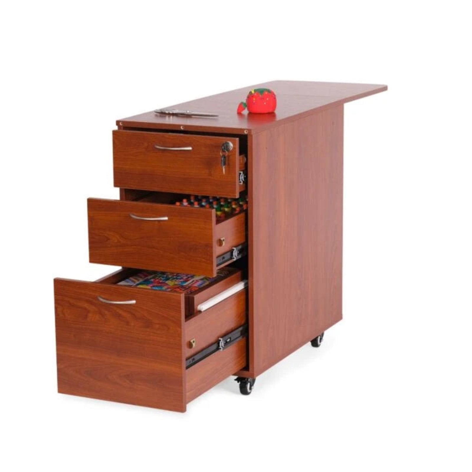 A reddish-brown wooden rolling file cabinet with three drawers, two of which are open, showing colorful items inside. It has a desktop surface with a small red object on top and is mounted on black caster wheels, photographed against a plain white background.
