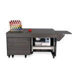 Sewing machine on a large dark wooden worktable with drawers and spools of thread.