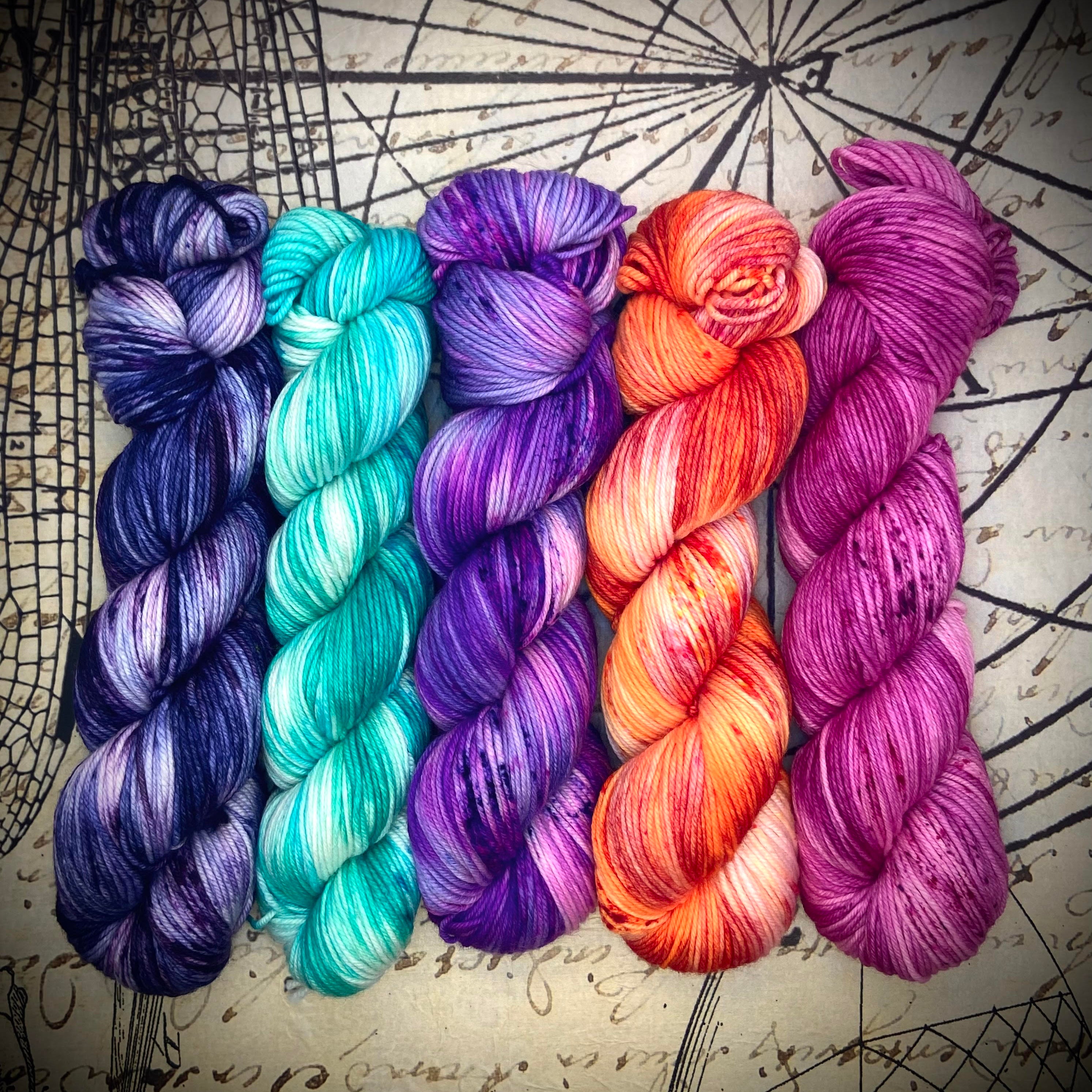 Five hand‑dyed yarn skeins in a fade set featuring blue, turquoise, purple, orange, and magenta tones.