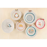 Six small white woven baskets with colorful printed designs and small brown leather handles, arranged on a light beige background. (not included with the embellishment kit)