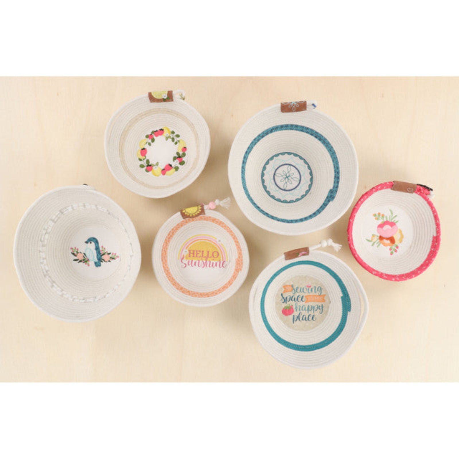 Six small white woven baskets with colorful printed designs and small brown leather handles, arranged on a light beige background. (not included with the embellishment kit)