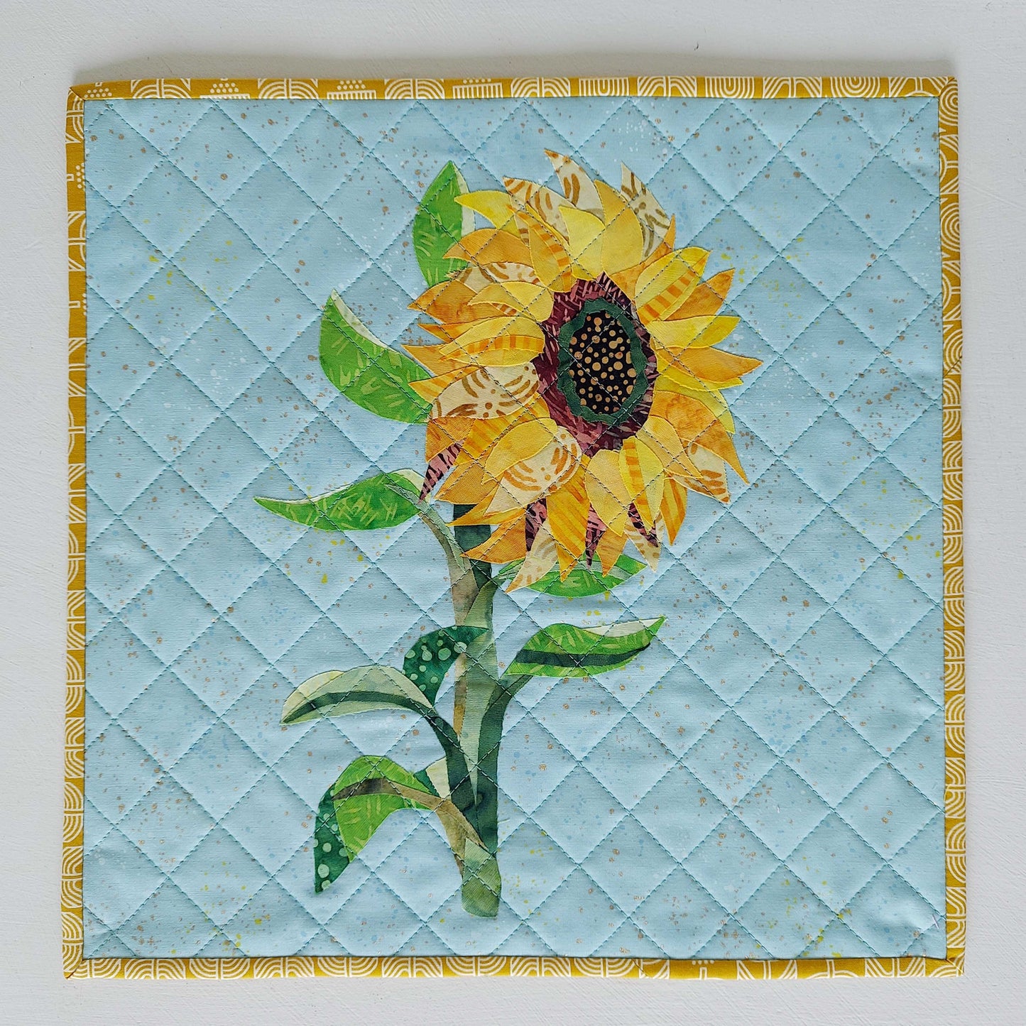 Sunflower collage created with layered fabric pieces using the parchment pressing technique, taught by instructor Kim Andersen.