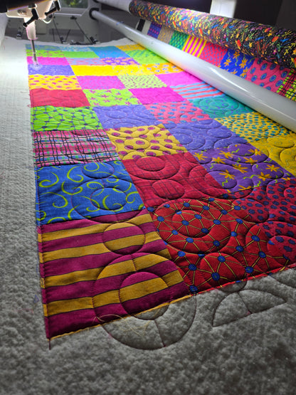 Longarm quilting machine stitching curved patterns across a colorful patchwork quilt