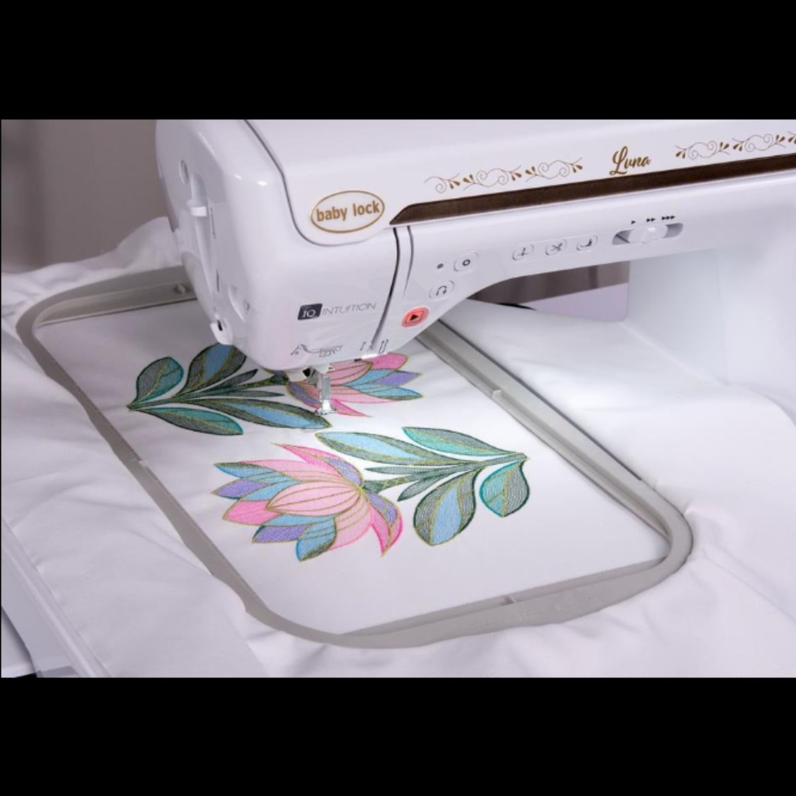 A white Baby Lock Luna embroidery machine stitching a colorful floral design inside a circular embroidery hoop on white fabric.