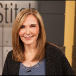 Headshot of Peggy Sagers wearing a blue top and dark cardigan, with the Fit‑2‑Stitch logo blurred in the background.