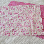 Two coordinating pillowcase fabrics laid flat on a white quilted surface, showing pink and white prints.
