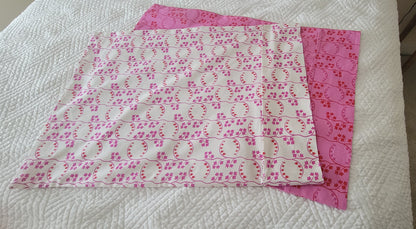 Two coordinating pillowcase fabrics laid flat on a white quilted surface, showing pink and white prints.