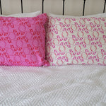 Two handmade pillowcases in coordinating pink and red prints, propped upright against a black metal bedframe.